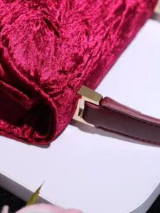 Red velvet handbag detail view, elegant textured clutch purse with gold hardware.