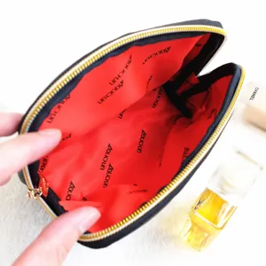 Detailed close-up view of black leather cosmetic bag featuring red interior lining and gold zipper.