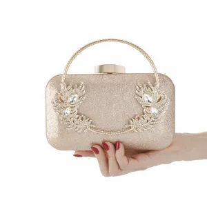 Close-up of sparkling gold evening clutch bag with rhinestone feather design and round handle.