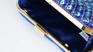Close up detail of blue rhinestone evening clutch bag with gold metal frame and satin lining.