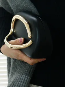 Close-up detail of the elegant black evening clutch with unique gold metal handle design.
