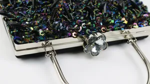 Close-up detail of luxury black sequin evening bag with sparkling crystal flower clasp and metal frame.