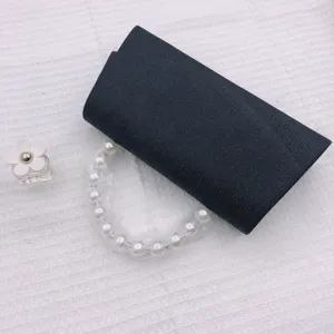 Black evening clutch bag detail showcasing textured fabric and elegant pearl handle design.