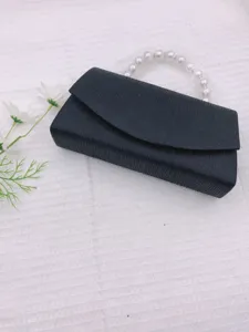 Black evening clutch bag detail with elegant pearl handle for wedding party dress accessories.