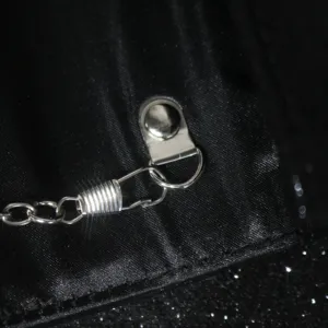 Close-up detail of the metal hardware, silver chain and clasp on a black evening bag.