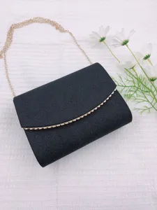 Détail de sac de soirée pailleté noir avec bandoulière chaîne et texture scintillante.