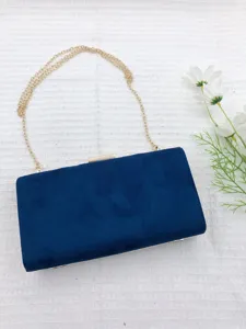 Detail view of a stylish deep blue velvet box clutch bag featuring a sleek gold chain strap.