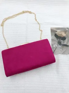 Detail view of the fuchsia suede evening clutch bag featuring a gold chain strap and clasp.