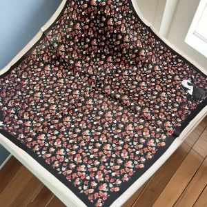 Detailed view of black silk small square scarf featuring vibrant red floral pattern and chic border.