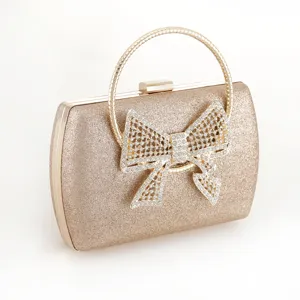 Gold glitter evening clutch bag detail showing rhinestone bow and round metal handle design.