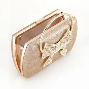 Gold glitter evening clutch bag with rhinestone bow and metal ring handle detail view.
