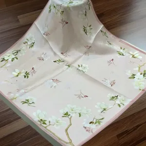 Detail view of the silk square scarf featuring delicate white floral print and pink border.