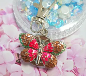 Detail shot of a gradient butterfly pocket watch keychain with pink and brown enamel.