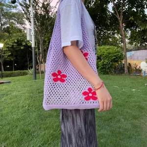 Detailansicht einer lila Häkel-Netz-Tragetasche mit rotem Blumenmuster im Freien.