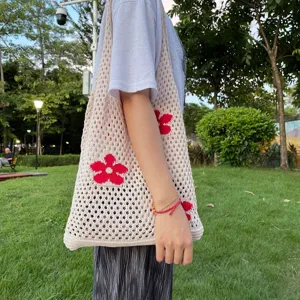 Detailansicht einer beige geflochtenen Häkel-Tasche mit rotem Blumenmuster im Park.