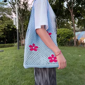 Detailaufnahme der blauen Häkel-Umhängetasche mit rosafarbenem Blumenmuster im Außenbereich.
