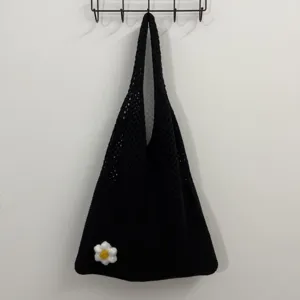 Nahaufnahme der schwarzen Häkel-Stofftasche mit handgemachter Gänseblümchen-Blüte an der Wand.