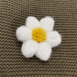 Handgemachte Strickwollblume Detailaufnahme, süßes weißes Gänseblümchen für Taschen und Kleidung.