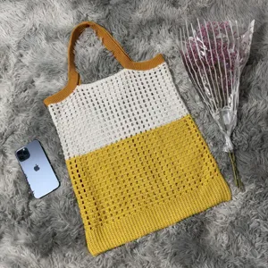 Detailansicht der gehäkelten Beuteltasche im Farbblock-Design, stilvoll auf einem flauschigen Teppich.