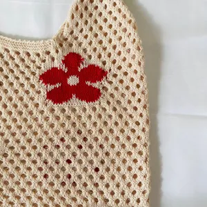 Nahaufnahme Detail der beige gestrickten hohlen Mesh Tragetasche mit rotem Blumenmuster.