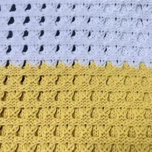 Nahaufnahme Detail der gestrickten hohlen Mesh-Stofftextur mit weiß-gelbem Farblock-Design.