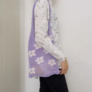 Close-up of purple crochet tote bag with white flower patterns worn on shoulder for daily use.