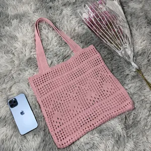 Detailansicht einer rosa Strick-Tragetasche mit Netz-Häkelstruktur in einer gemütlichen Szene.