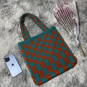 Detailaufnahme einer grün-orange karierten Strick-Tragetasche auf einem flauschigen Teppich.