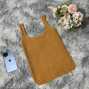 Nahaufnahme der gelben Häkel-Strick-Tasche, flach auf flauschigem Teppich mit Blumen.