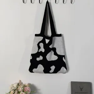 Gros plan sur le sac fourre-tout en tricot noir et blanc avec motif vache et anses solides.