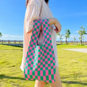 Detailaufnahme einer stylischen rosa-grünen Strick-Karomustertasche im Freien auf Rasen.