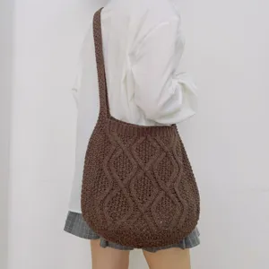 Detailansicht einer dunkelbraunen Strick-Tasche mit Zopfmuster am Körper getragen.