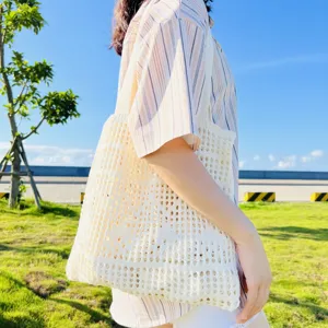 Nahaufnahme einer beige gestrickten Lochmuster-Umhängetasche im sonnigen Park.