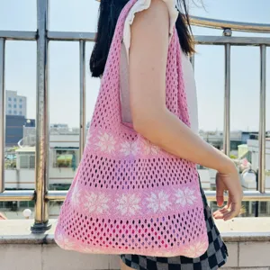 Detailaufnahme einer rosa Strick-Netz-Tasche mit Blumenmuster, legerer Outdoor-Stil.