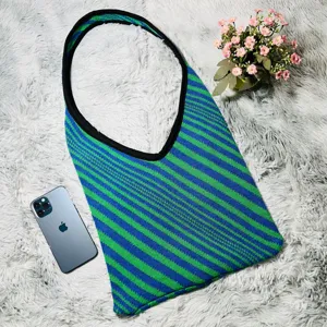 Scatto dettagliato di borsa a tracolla in maglia a righe blu e verdi su tappeto bianco soffice.