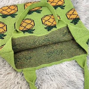 Close-up view of a green knit tote bag featuring a playful pineapple pattern and knit texture.