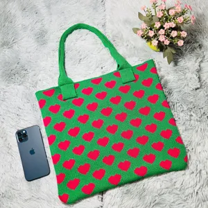 Grüne Strick-Tragetasche mit rosa Herzmuster, Detailansicht zeigt Stricktextur und flaches Design.