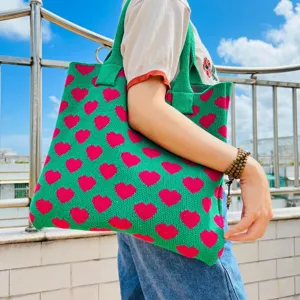 Detailansicht der gestrickten Tasche mit grünem Stoff und rosa Herzen unter dem blauen Himmel.