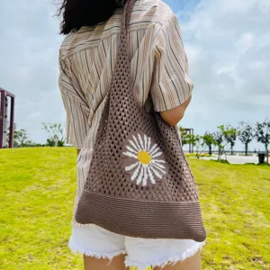 Nahaufnahme der braunen gestrickten Schultertasche mit Lochmuster und süßem Gänseblümchen-Design.