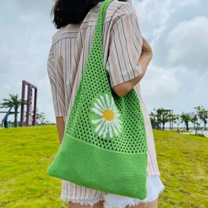 Detailaufnahme einer gruenen gehakelten Umhaengetasche mit weissem Bluemchen im Freien.