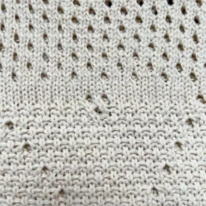 Nahaufnahme des beigen Strickstoffs mit weicher Textur und feinem Flechtmuster-Design.