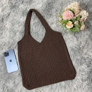 Braune gestrickte Tasche Detailansicht, ästhetisches Flatlay mit Blumen auf flauschigem Teppich.