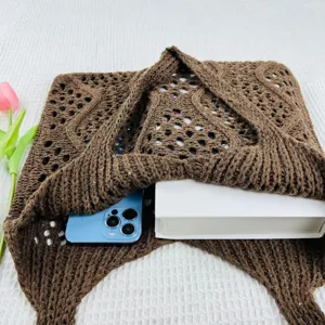 Detailansicht der braunen hohlen Strick-Tasche mit Buch und Handy auf weißer Textur.