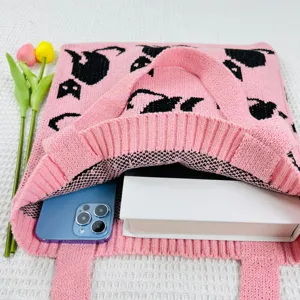 Nahaufnahme der rosa Strick-Tragetasche mit niedlichem schwarzem Katzenmuster und Smartphone-Detail.