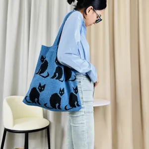 Detailansicht einer blauen Strick-Tasche mit schwarzen Katzenmotiven, getragen vom Model innen.
