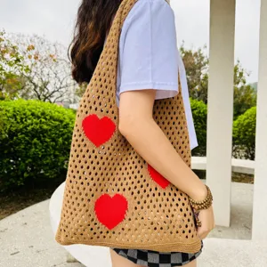 Detailaufnahme einer braunen Strick-Shopper-Tasche mit rotem Herzmuster im Lochmuster.
