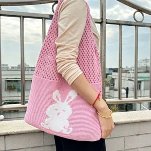 Nahaufnahme einer rosa Strick-Tragetasche mit weißem Hasenmuster auf der Schulter.