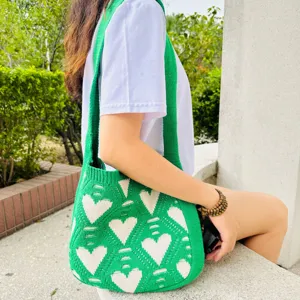 Primer plano detalle del bolso shopper de punto verde con diseño de corazón al aire libre.