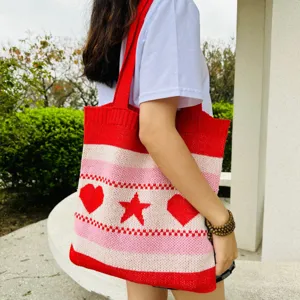 Detailaufnahme einer stylischen rot-pinken Strick-Tote-Bag mit Herzen und Sternen im Freien.