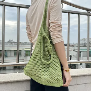 Detailansicht der grünen Strick Netztasche am Körper getragen, zeigt die offene Webstruktur.
